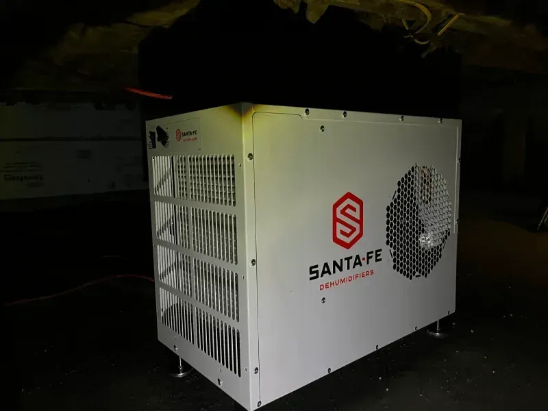 A white Santa Fe dehumidifier standing in a dark basement.