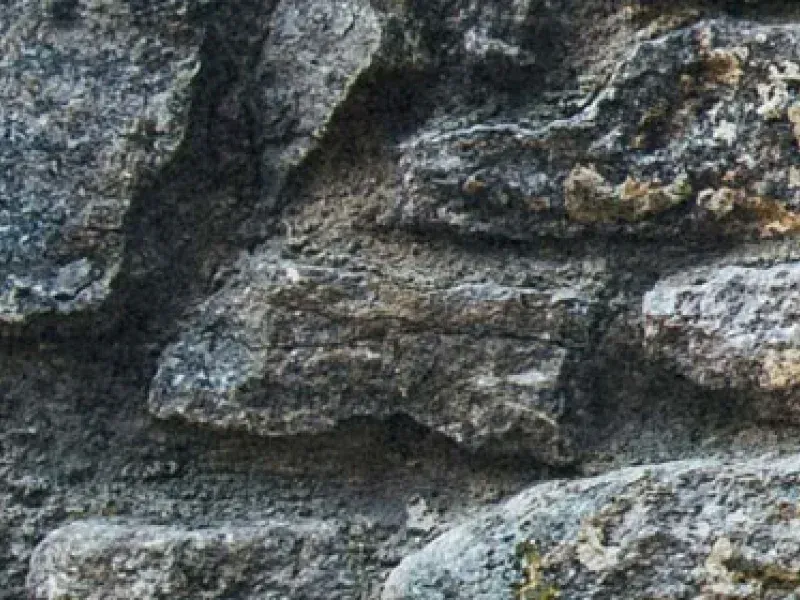 A close-up view of textured, rough grey stone masonry with visible mortar gaps.