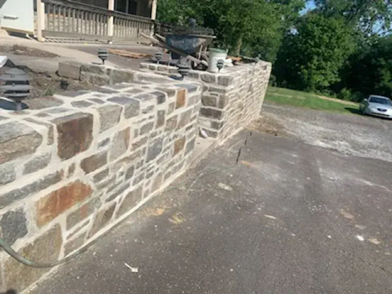 A newly constructed fieldstone retaining wall borders a paved driveway in front of a house.