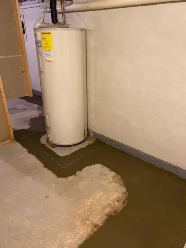 A water heater sits in a basement corner where a large, shallow pool of brown water covers the concrete floor.
