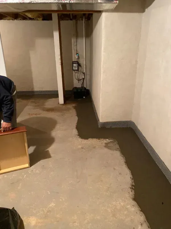 Basement floor showing a fresh concrete patch along the wall near a sump pump and mechanical equipment.
