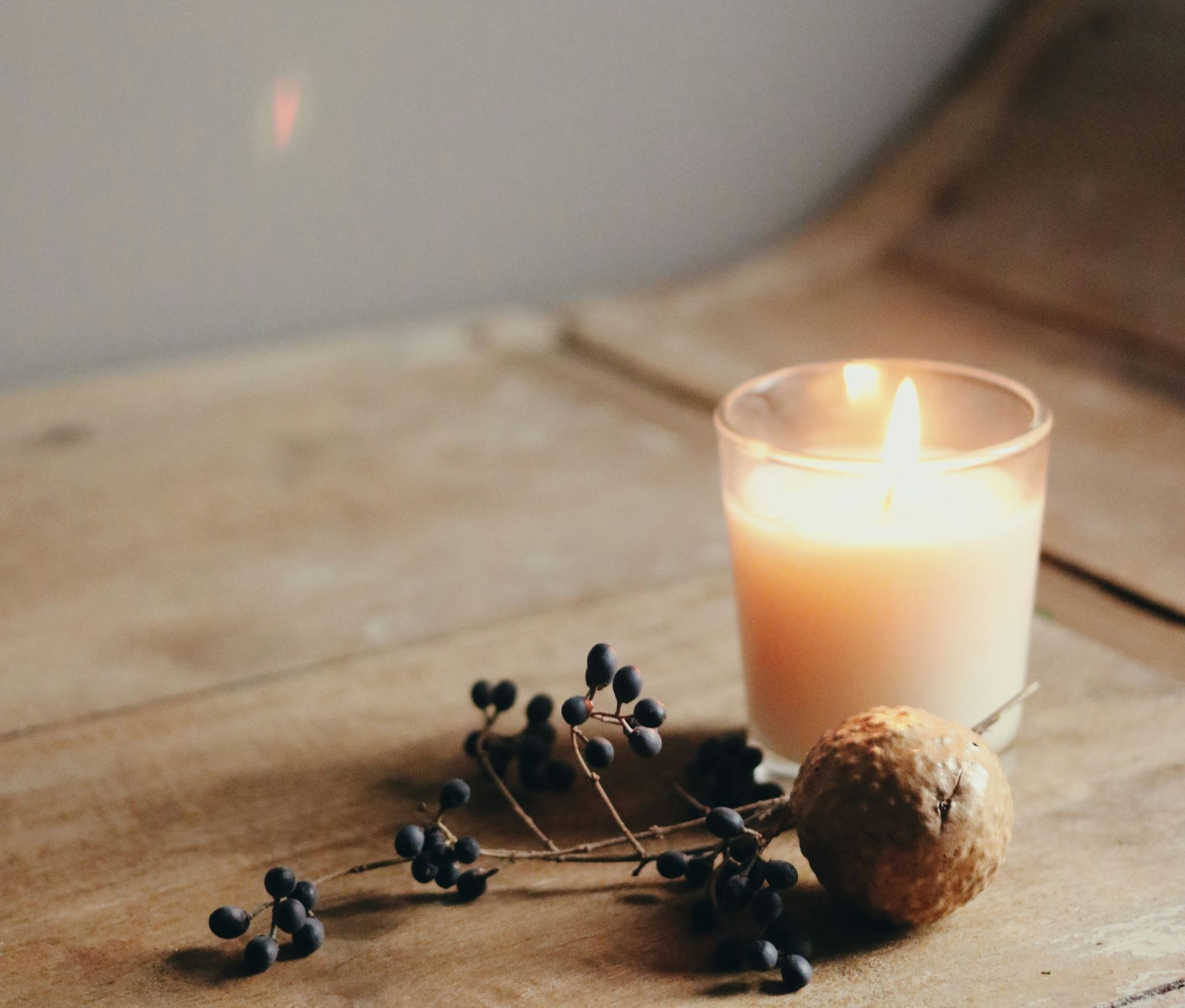 Lit candle in a glass with dried berries and a small gold ornament on a wooden surface