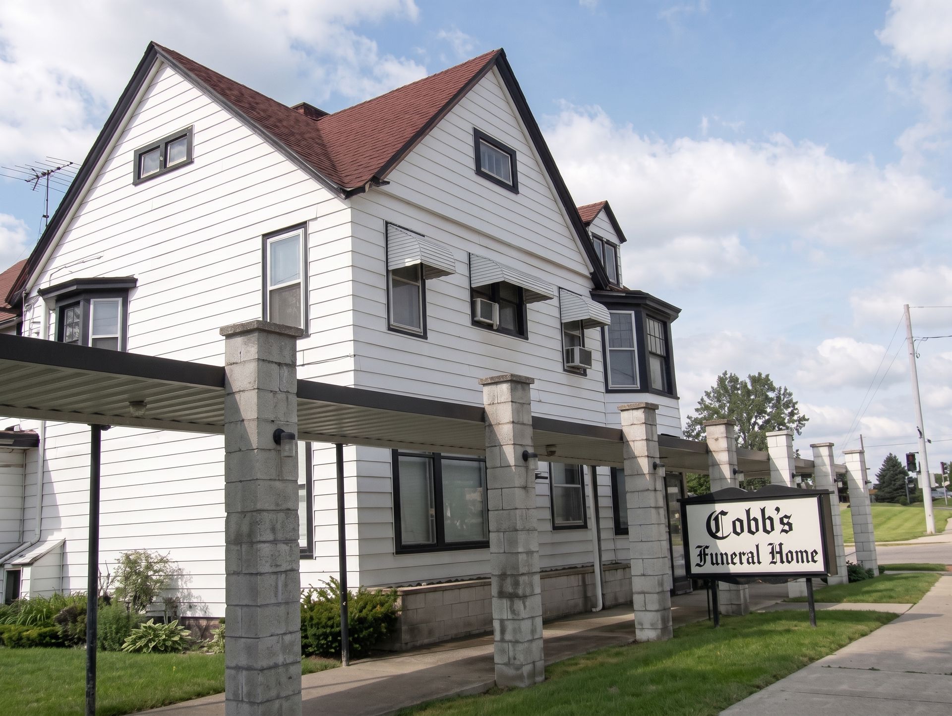 Cobb’s Market house-style storefront with white siding, red roof, and stone posts under a partly cloudy sky