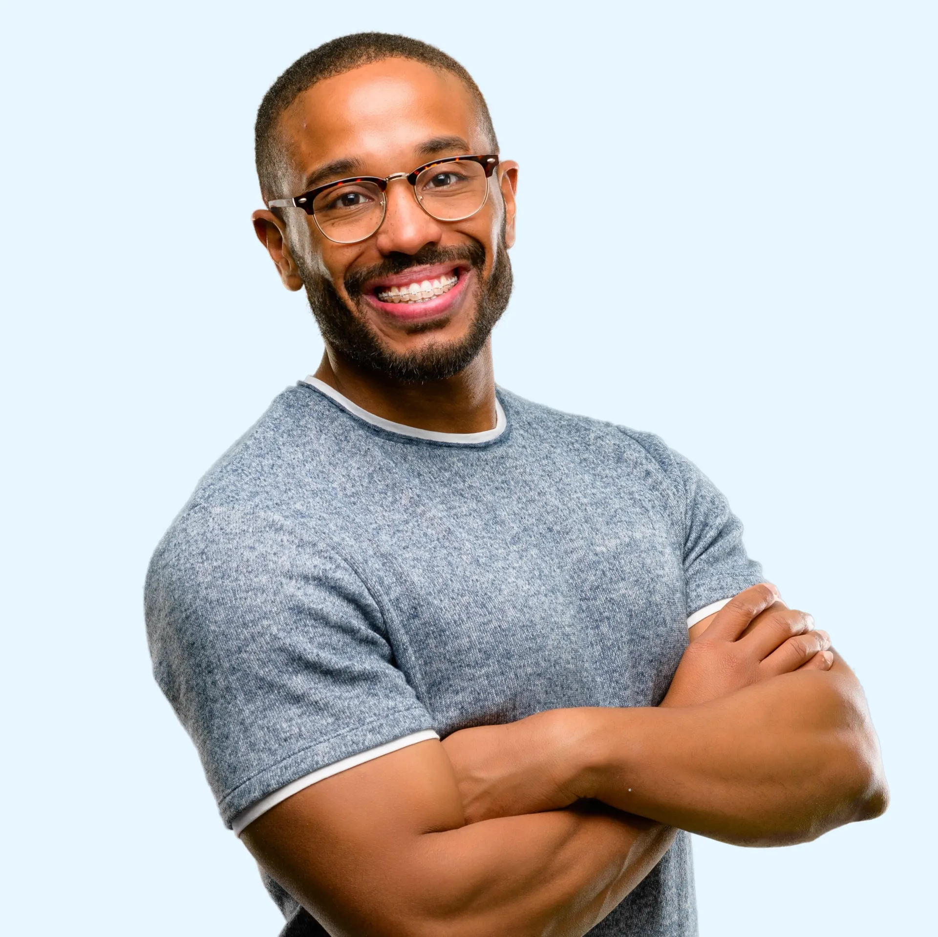 A man with braces and wearing glasses is smiling with his arms crossed.