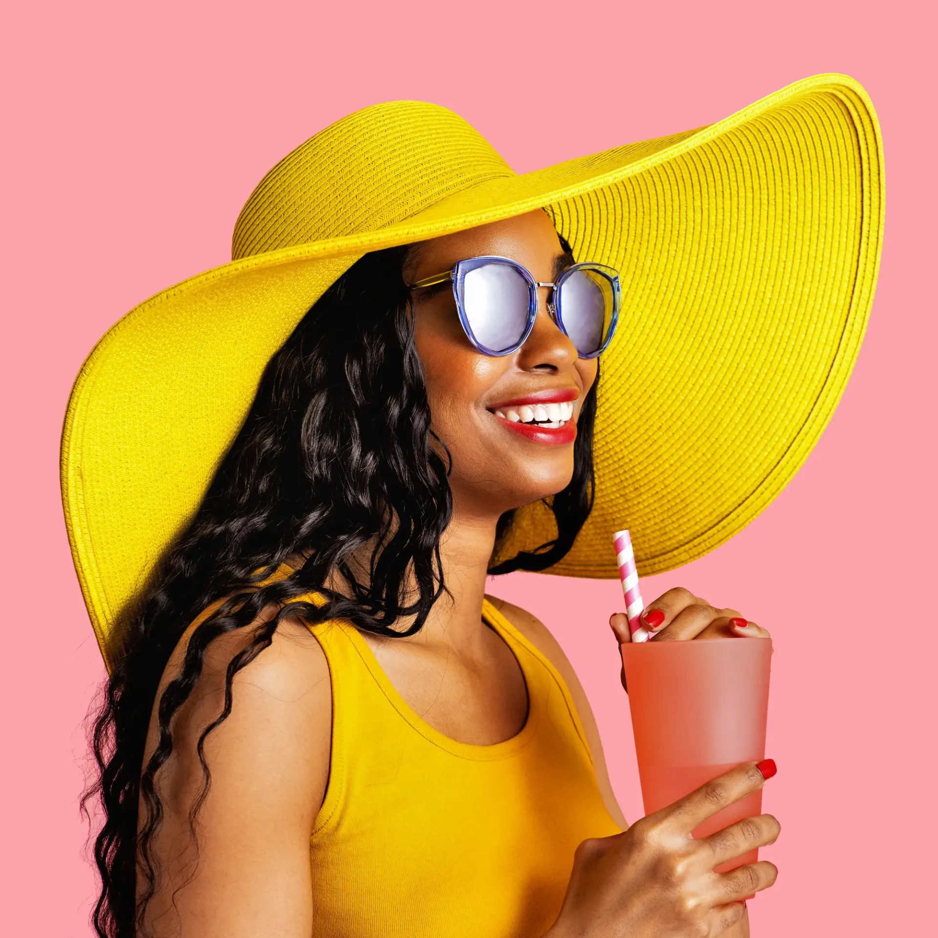 A woman wearing a yellow hat and sunglasses is drinking a drink through a straw.