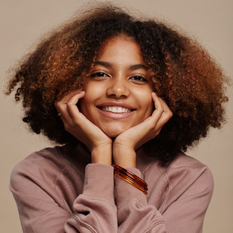 A woman with curly hair is smiling with her hands on her face.
