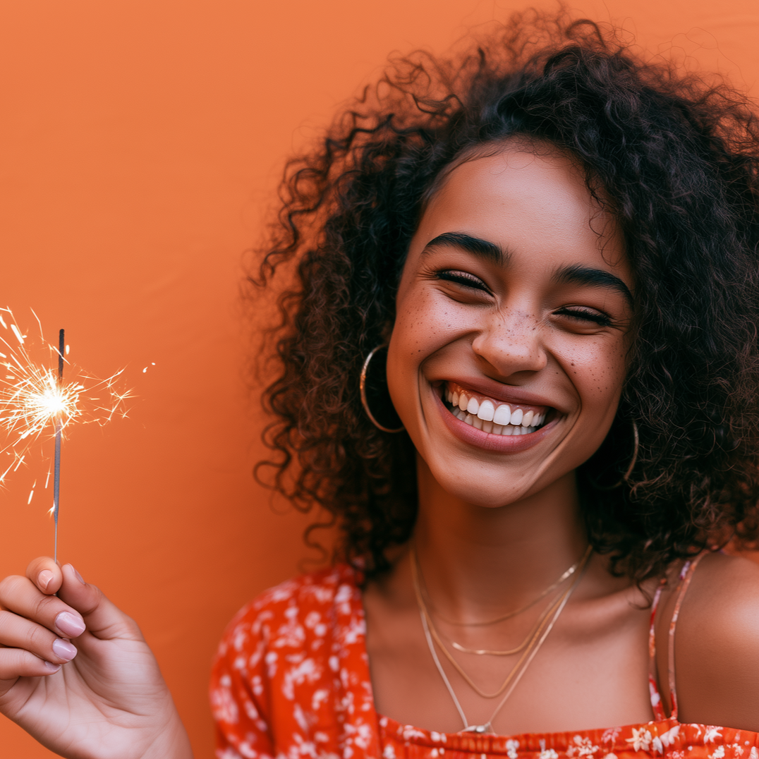 Smiling woman holding a lit sparkler against an orange background