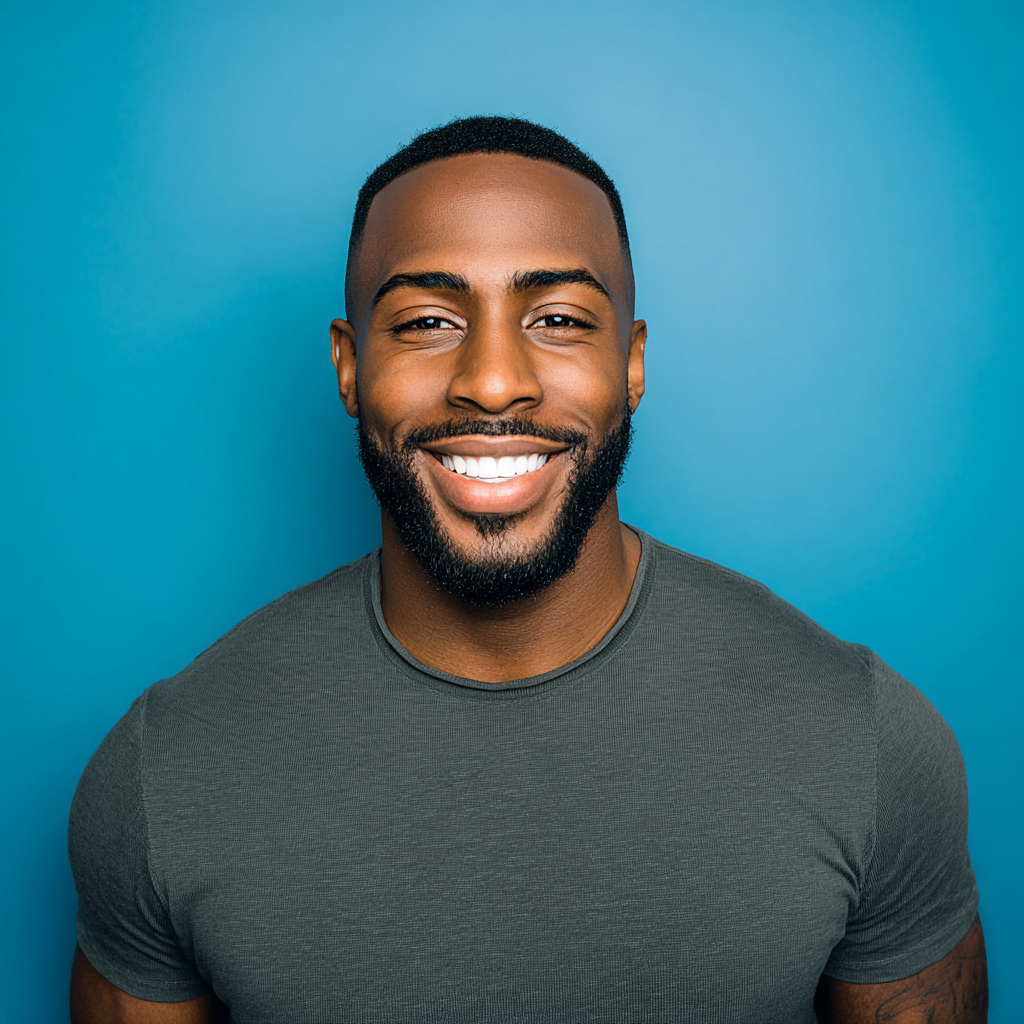 Smiling man with dark skin, wearing a gray shirt, against a blue background.