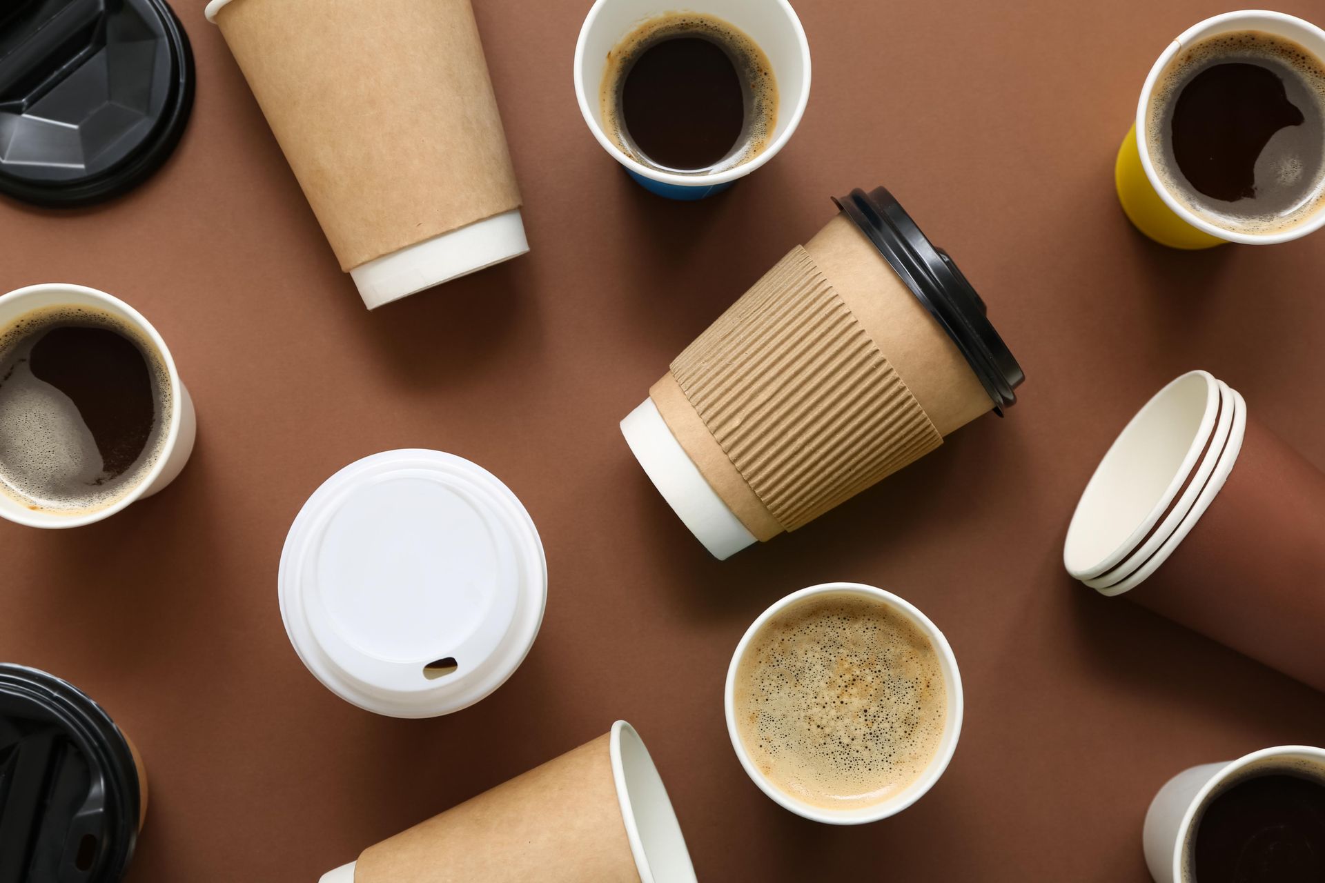 Overhead view of coffee cups on a brown surface; some filled, some with lids.