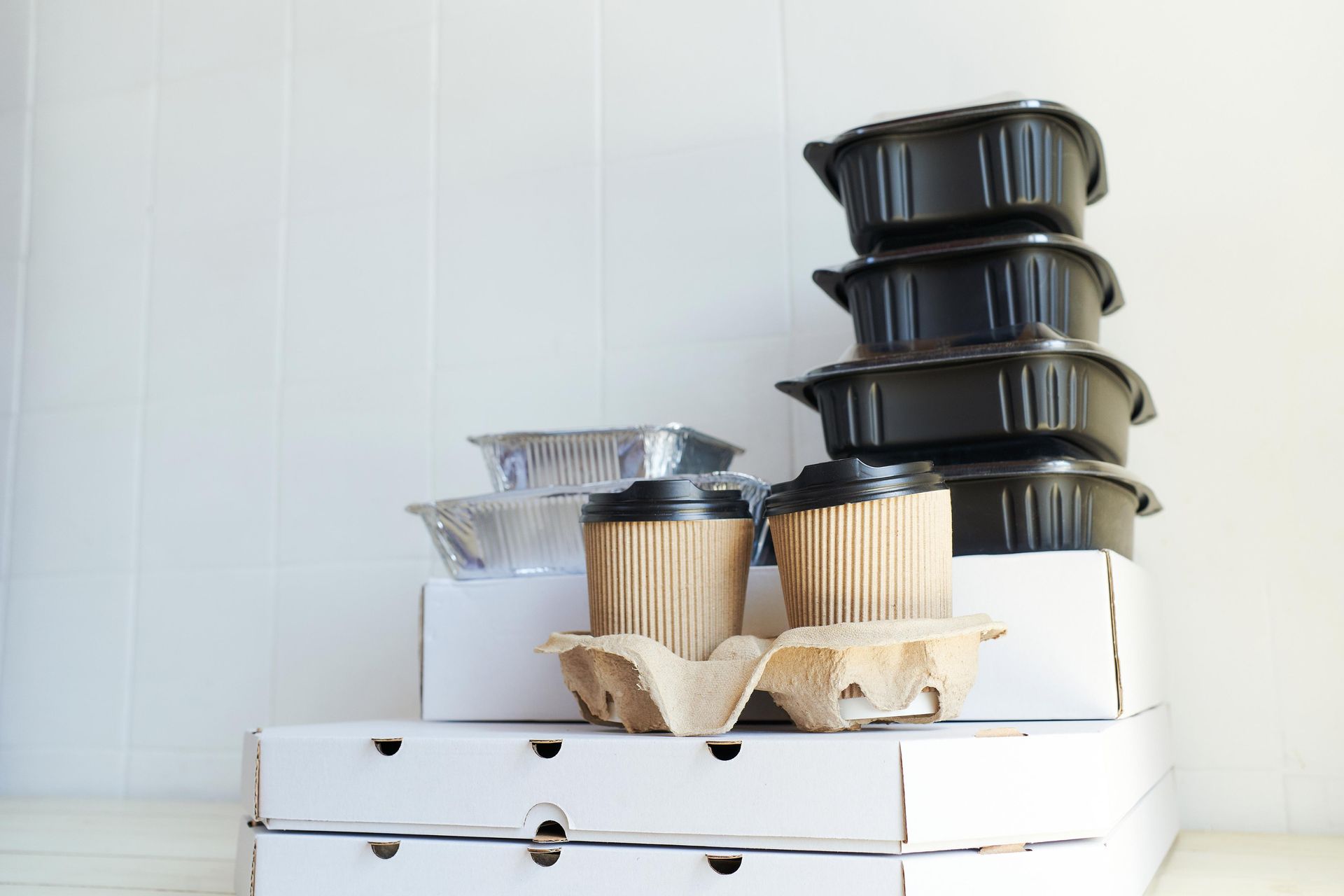 Takeout containers stacked on white boxes: food containers, coffee cups, pizza boxes.