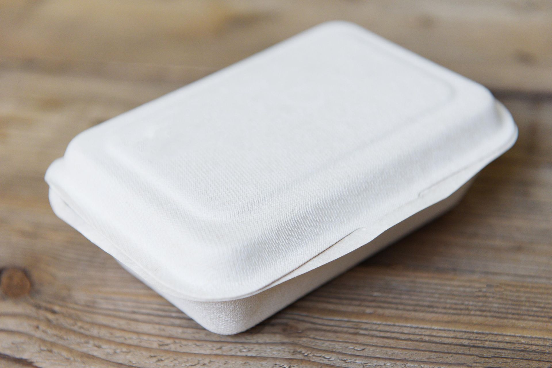 White, closed, rectangular takeout container on a wooden surface.