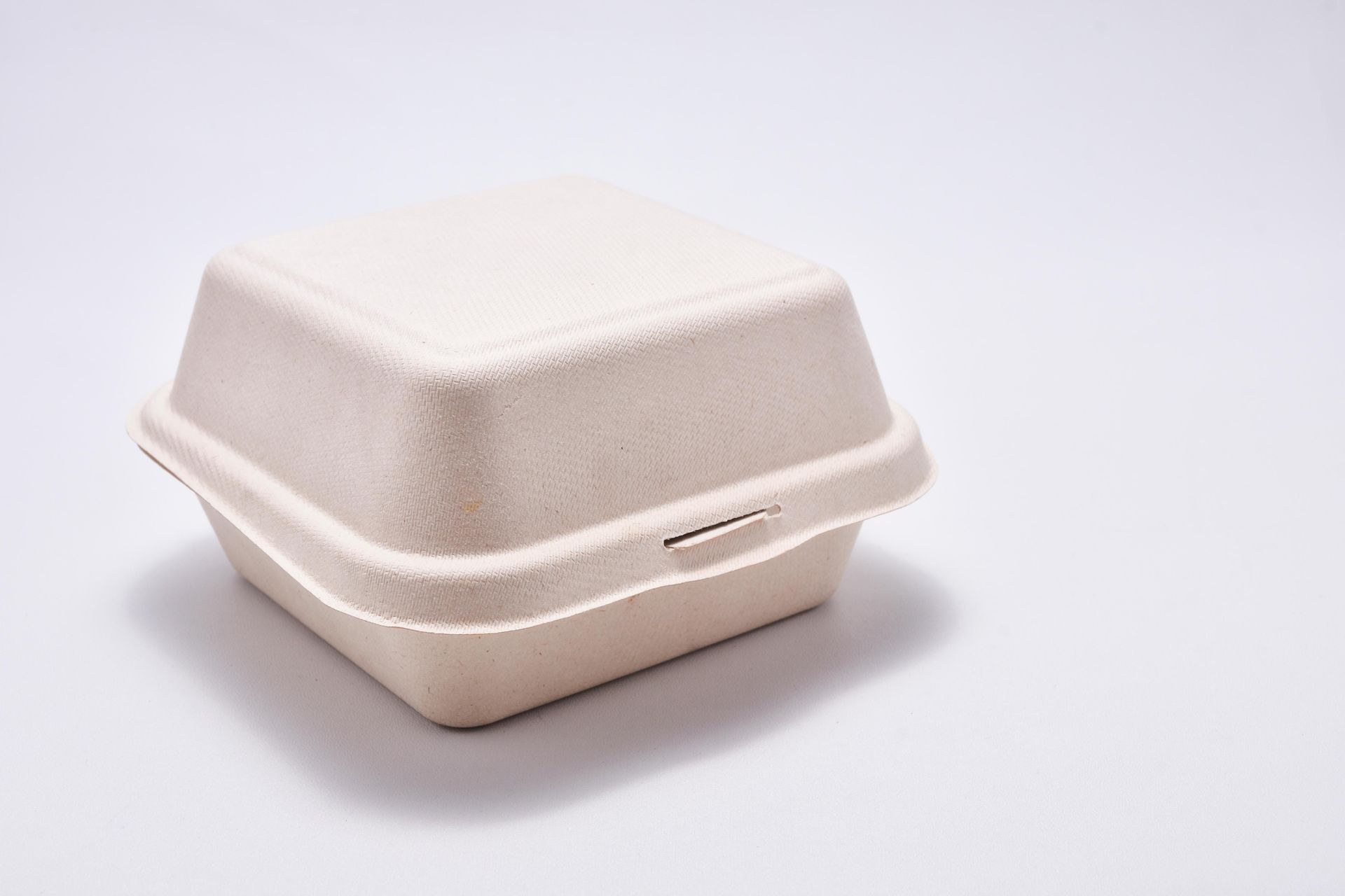 Closed, square, beige-colored takeout container on a white surface.
