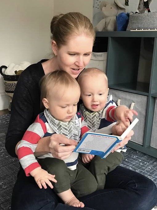 A postpartum doula reading a book to twin boys as their mom takes time to eat lunch