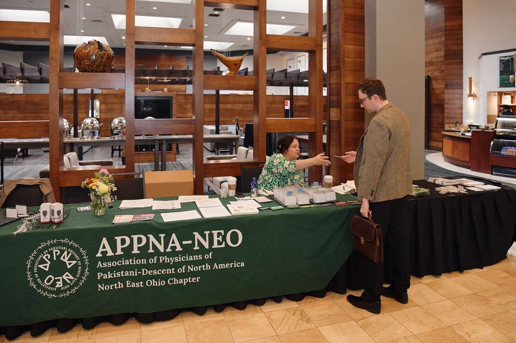 A person speaking at a podium in front of a circular banner featuring the flags of Ohio and Pakistan with the APPNA-NEO logo.