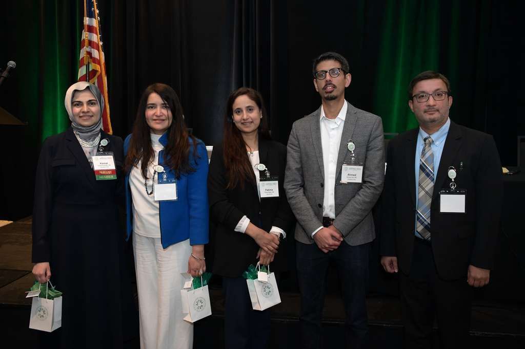 A group of people standing on a stage at an awards ceremony, holding certificates in front of a US-Pakistan emblem.