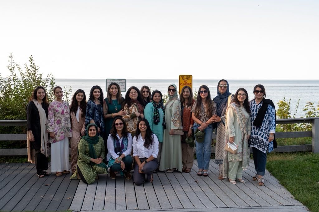 A large, diverse group of people posing for a group photo in front of academic research posters at a conference hall.