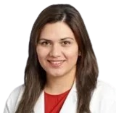 A smiling medical professional with long brown hair wearing a white lab coat over a red top against a gray background.