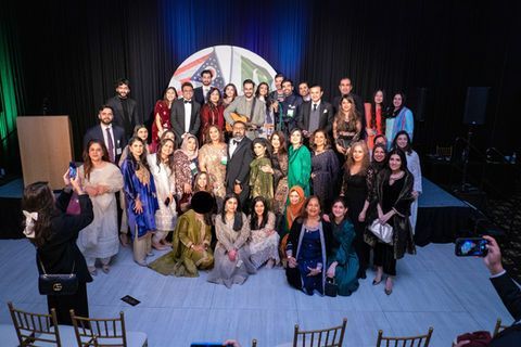 A group of people standing on a stage at an awards ceremony, holding certificates in front of a US-Pakistan emblem.