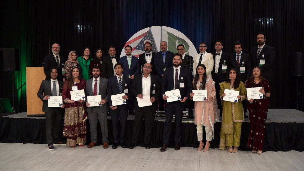 A large, diverse group of people posing for a group photo in front of academic research posters at a conference hall.