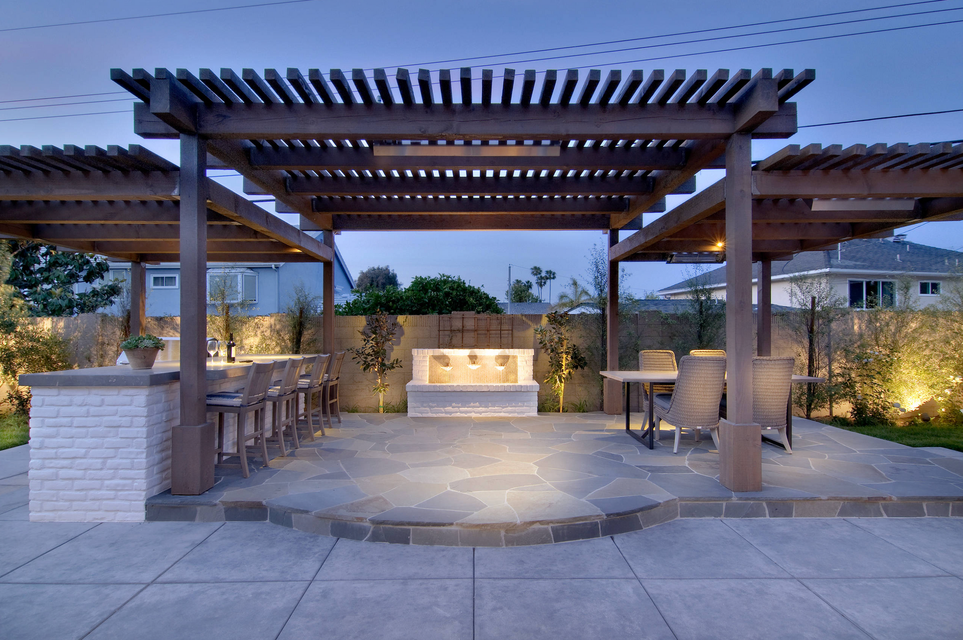 A patio with a pergola , tables , chairs and a fireplace.
