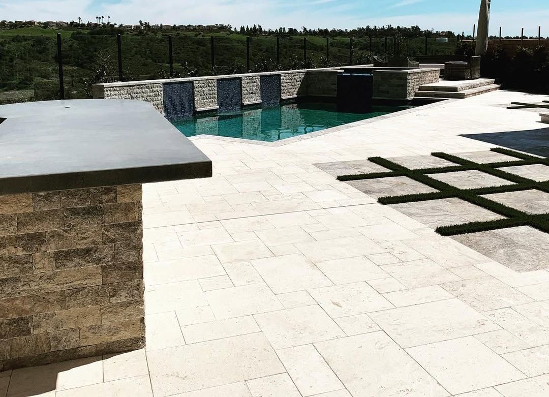 A large swimming pool is surrounded by a patio and a fence.