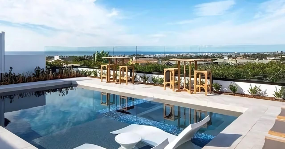 A large swimming pool surrounded by chairs and tables with a view of the ocean.