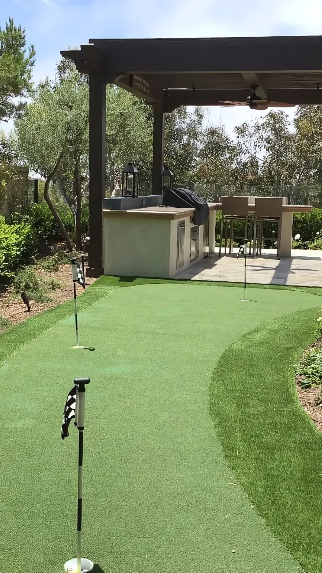 There is a putting green in the backyard with a pergola.