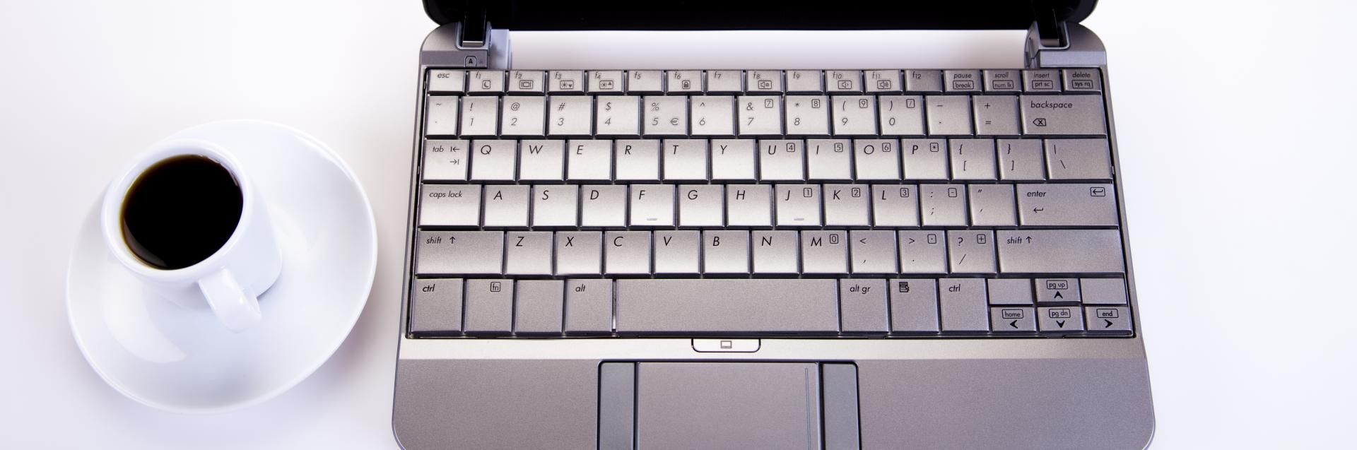 White coffee cup beside a silver laptop keyboard on a white desk
