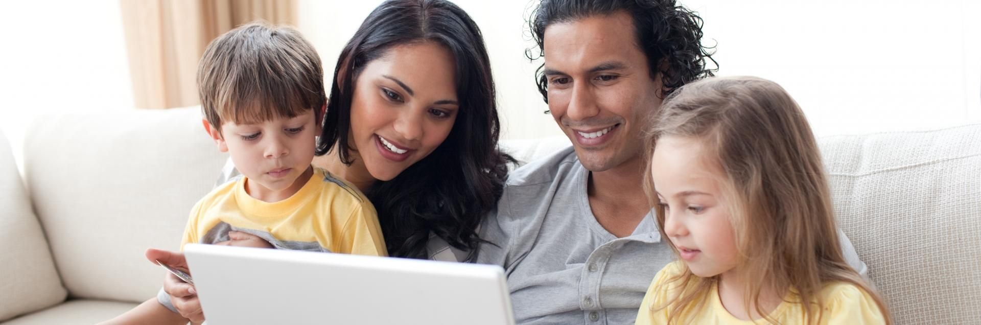 Family gathered on a couch, smiling and looking at a laptop together