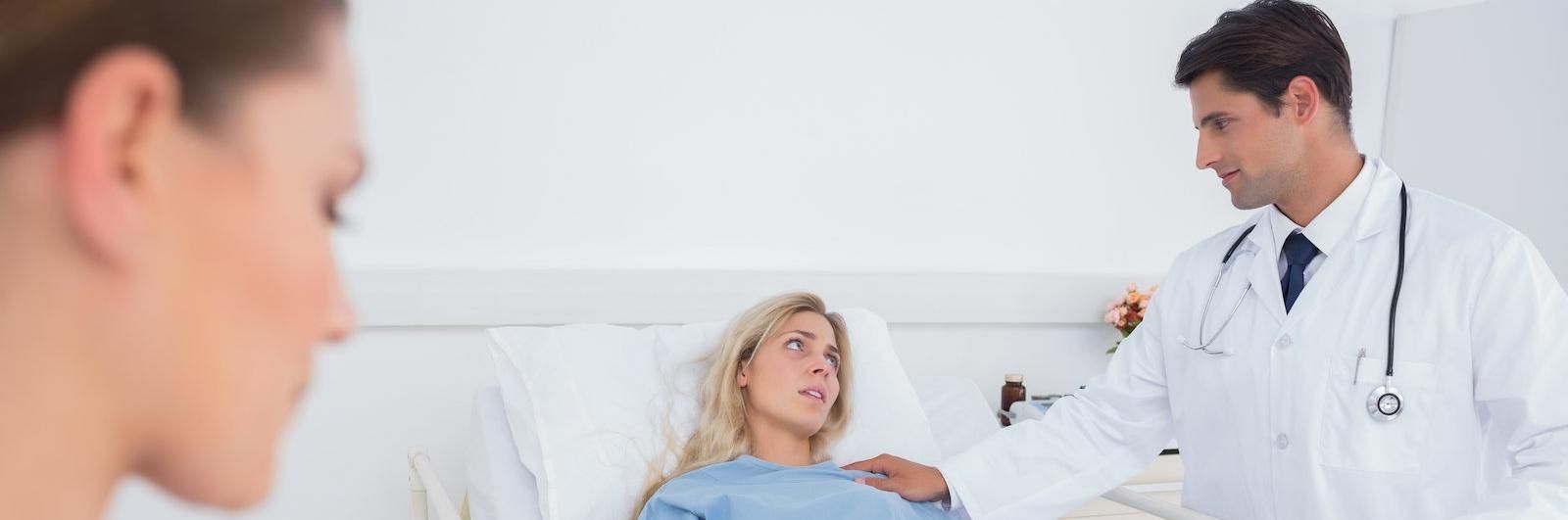 Doctor talking with patient in hospital bed while another person watches nearby