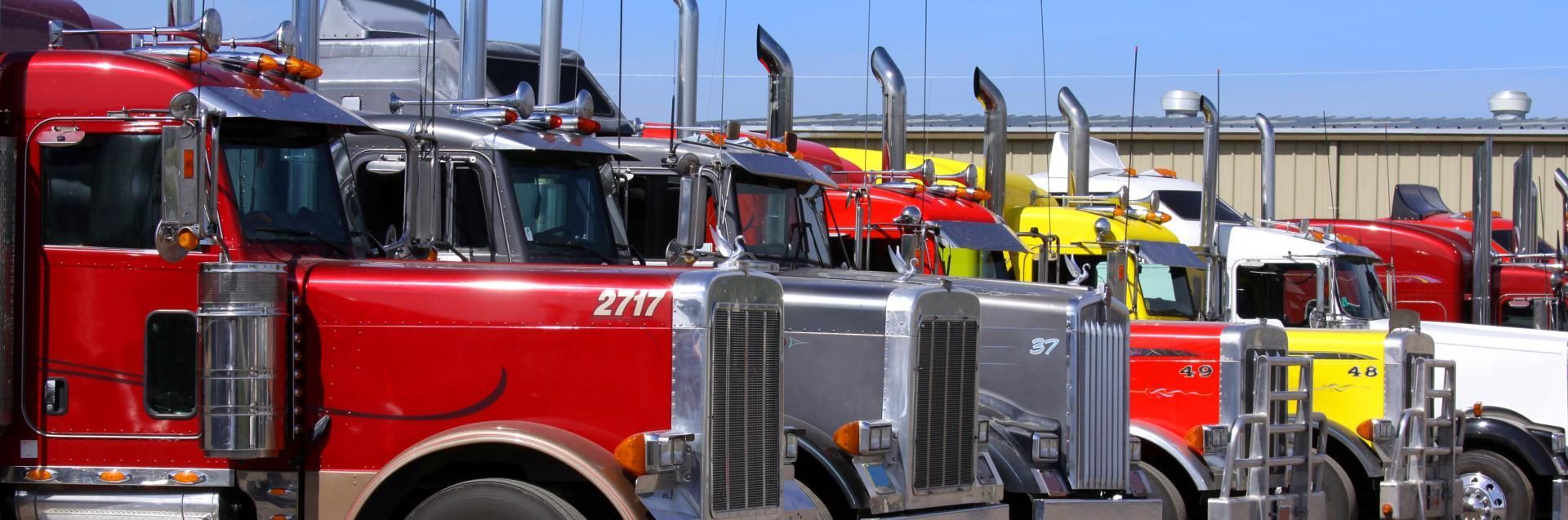 Row of shiny red and yellow semi trucks parked outdoors under a blue sky