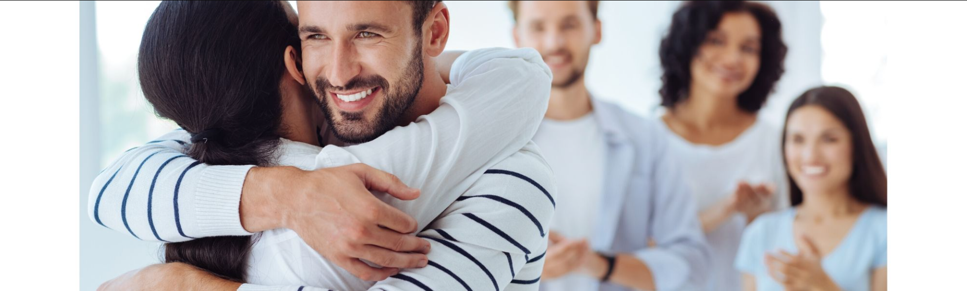 Smiling man hugging another person, with two blurred coworkers standing in the background