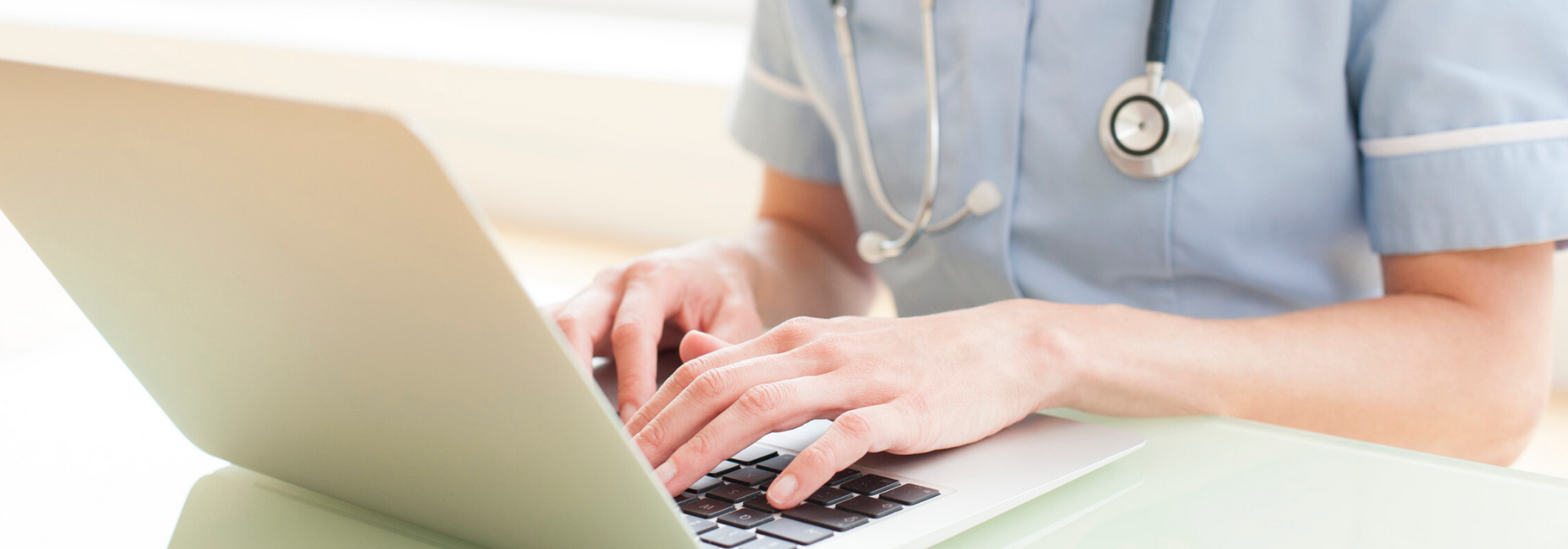 Healthcare worker typing on a laptop beside a stethoscope