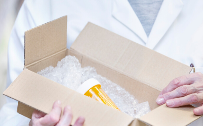 Open cardboard box with packing peanuts and a yellow item, hands holding the box open