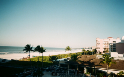 Tropical beachfront resort at sunrise with palm trees, ocean waves, and white buildings
