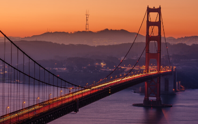 Golden Gate Bridge at dusk, lit in red-orange with city lights and foggy hills in the background