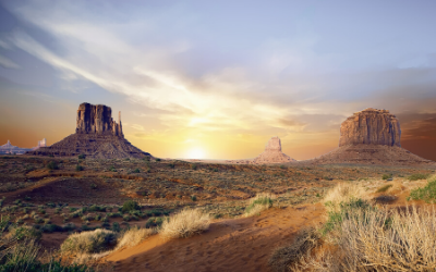 Sunrise over a desert landscape with red rock buttes and dry grass under a golden sky