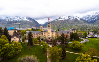 Historic castle-like building in a green valley with snowy mountains in the background