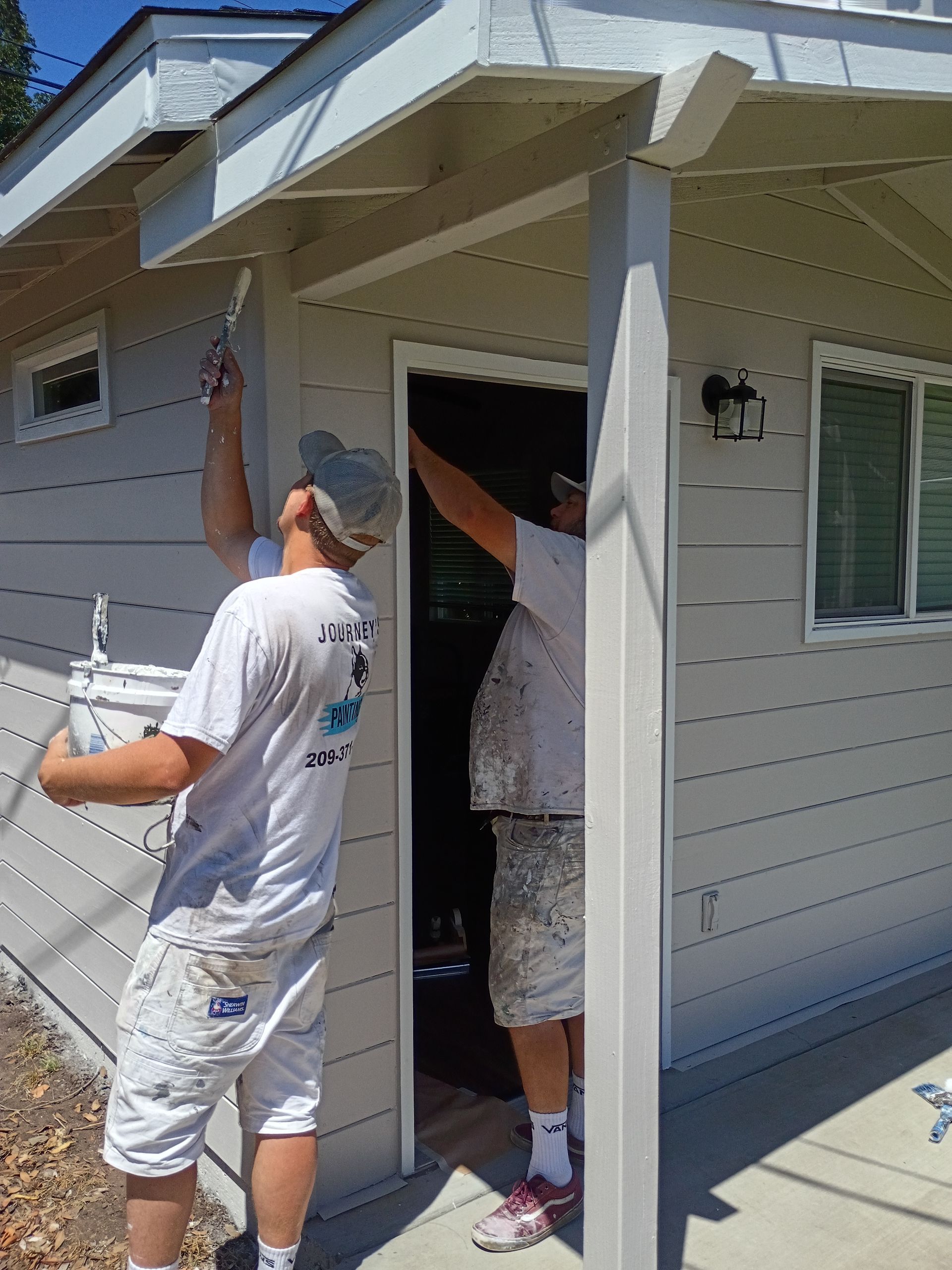 Person painting the exterior of a house near an open doorway and window.
