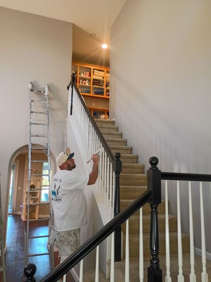 Painter in white coveralls touching up a stairwell wall beside a ladder and staircase