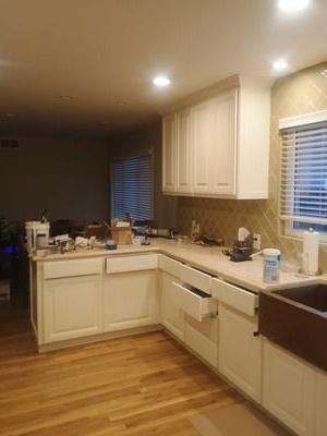 A kitchen with white cabinets, wood floors, and countertops cluttered with dishes and items under warm lighting.