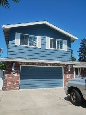Blue two-story house with brick lower level, white shutters, and a blue garage door under a clear sky