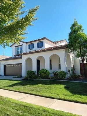 Suburban two-story house with white stucco, blue shutters, garage, and a green lawn under a clear blue sky