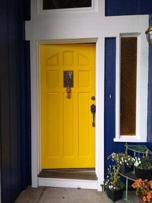 Bright yellow front door with a knocker, set in a blue house exterior with white trim.