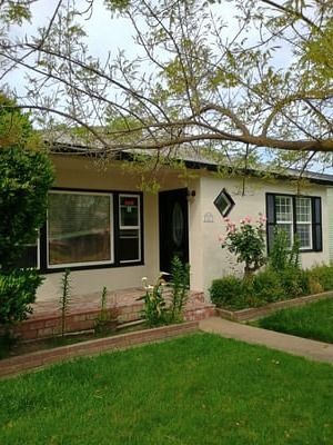 Single-story beige house with black trim, front lawn, walkway, and trees in the yard