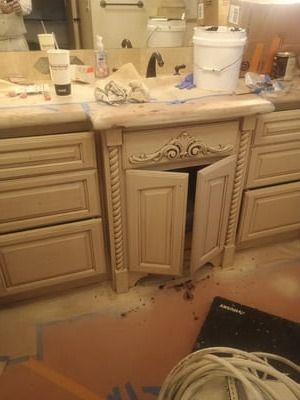 Damaged bathroom vanity cabinet with debris on the floor and countertop clutter nearby