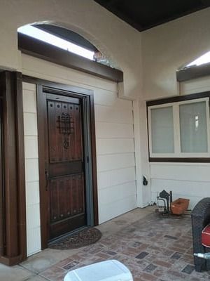 Front porch with dark wooden front door, white siding, window, and brick-patterned floor.