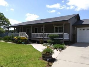 Single-story house with gray siding, front porch, lawn, and driveway under a blue sky