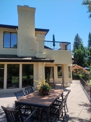 Modern two-story house with patio dining table, sliding doors, and a sunny backyard deck