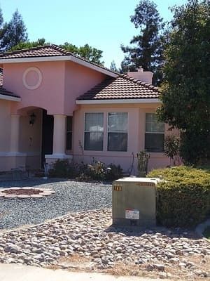 Pink stucco house with tiled roof, front yard landscaping, and a mailbox near the curb